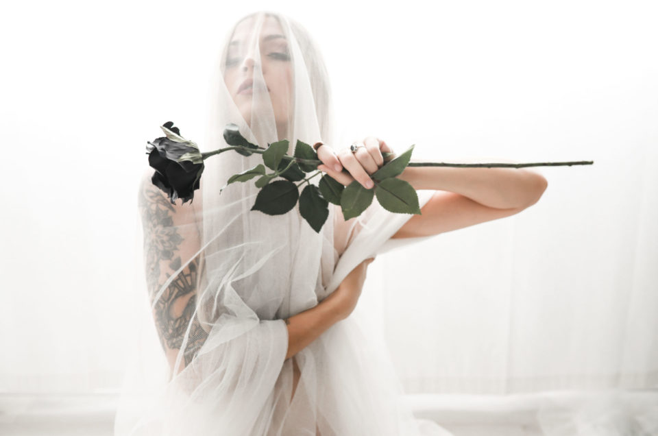 Woman-drapped-in-white-sheer-fabric-holding-a-black-rose