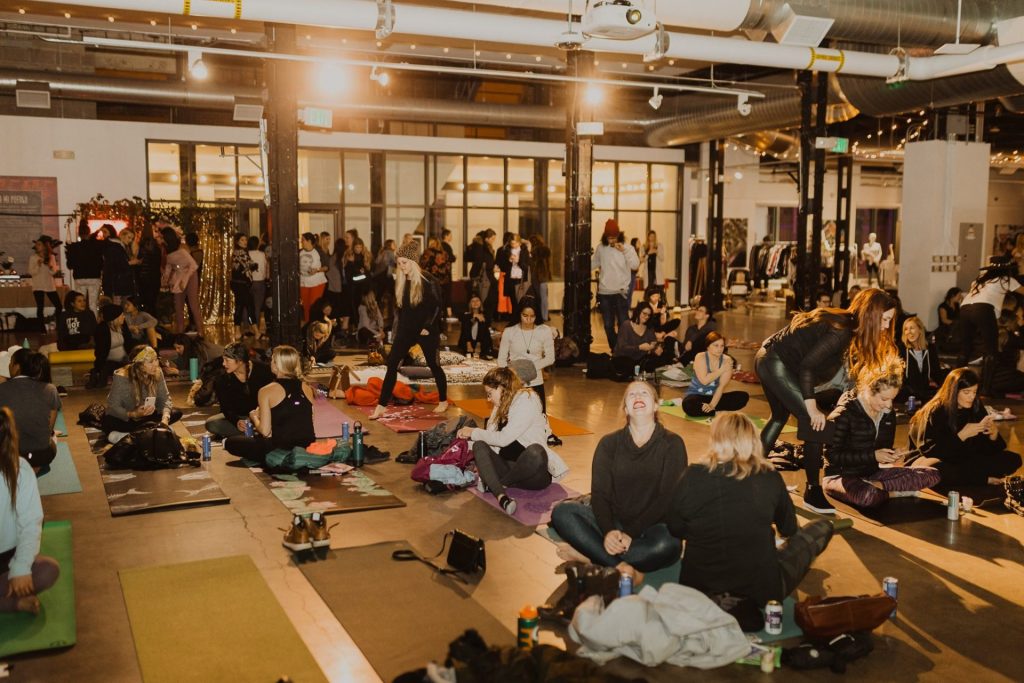 Large, open room full of women getting ready to do yoga.