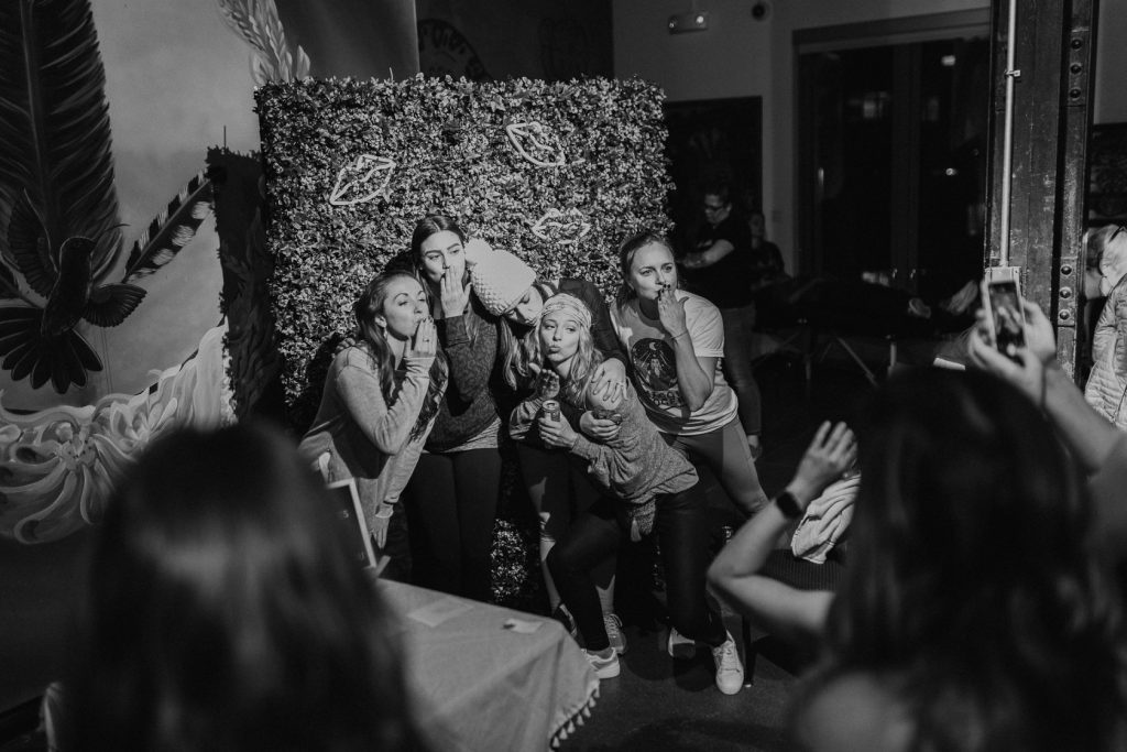 Five woman posing in front of a floral backdrop getting their photo taken.