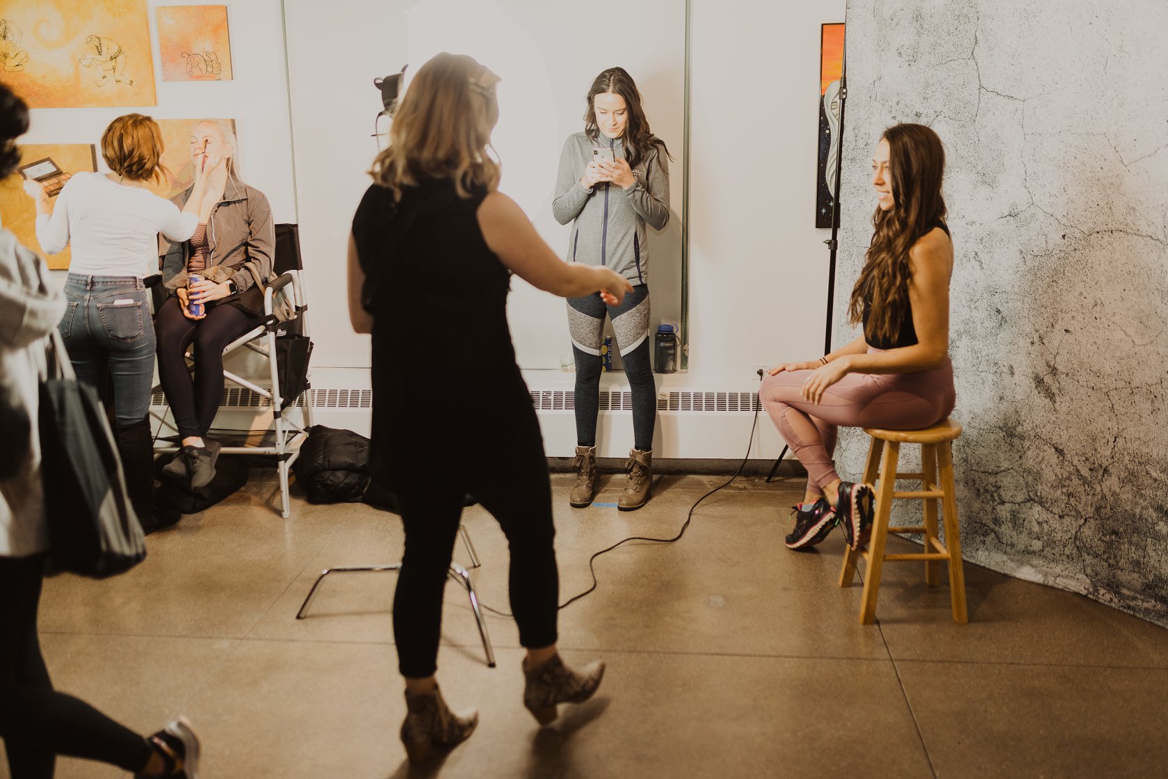 Woman photographer getting ready to take an image of a brown haired woman in a yoga outfit sitting on a wood stool at a Denver event.