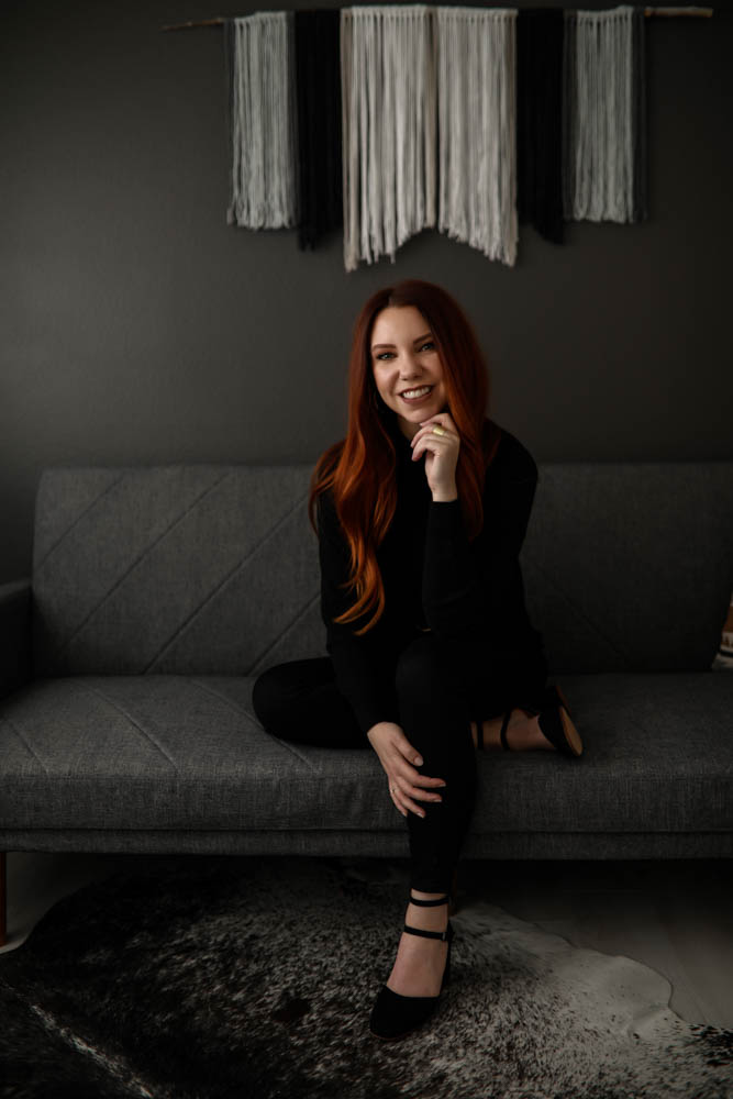 Denver-small-business-owner-with-long-red-hair-wearing-all-black-sitting-on-grey-couch-smiling