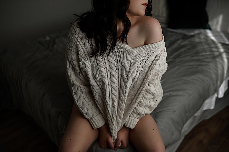 Boudoir-photos-of-dark-haired-woman-posing-on-a-bed-wearing-a-cream-colored-sweater