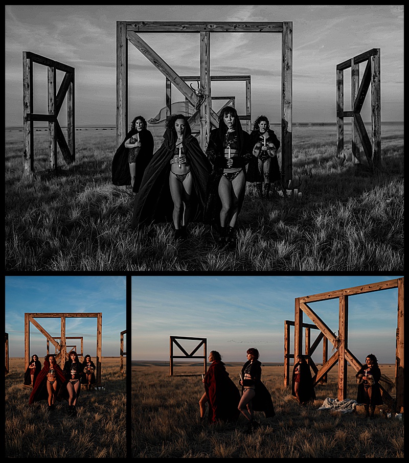 Witchy-women-dressed-in-lingerie-and-cloaks-posing-in-front-of-wooden-structures-in-the-middle-of-a-field