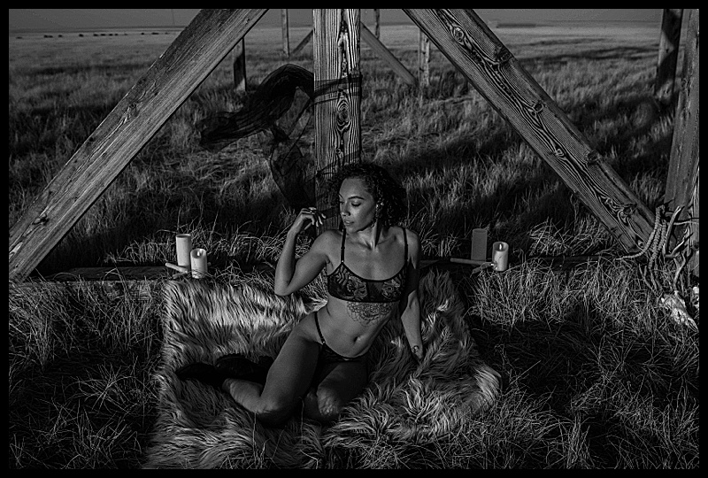 Witchy-women-dressed-in-lingerie-and-cloaks-posing-in-front-of-wooden-structures-in-the-middle-of-a-field