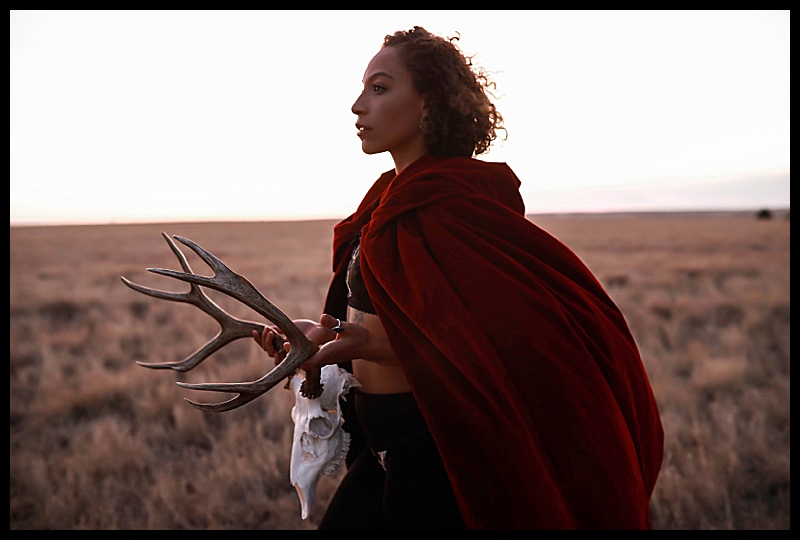 Witchy-women-dressed-in-lingerie-and-cloaks-posing-in-front-of-wooden-structures-in-the-middle-of-a-field