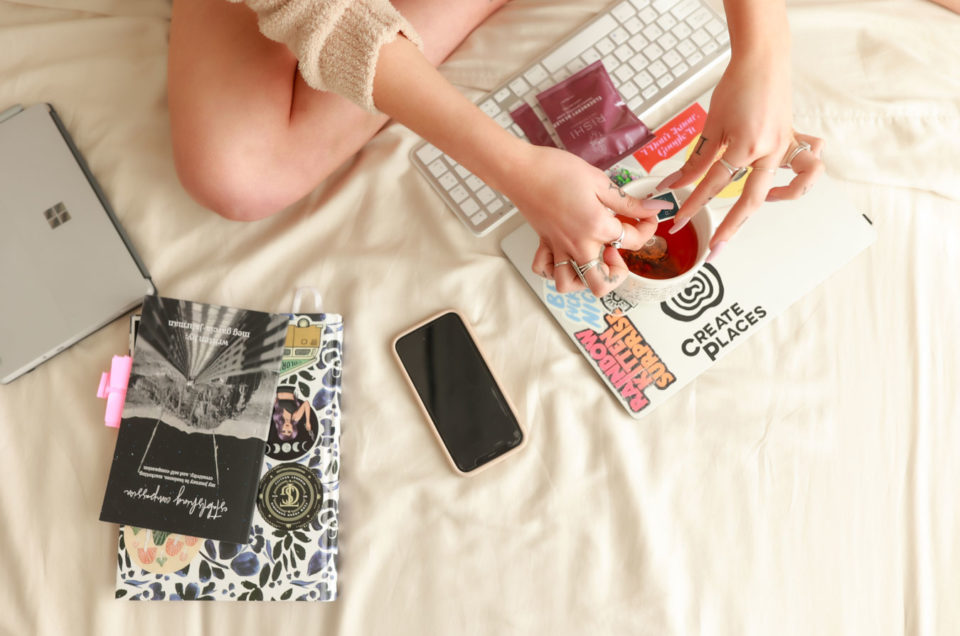 Overhead image of woman working on laptop in bed with a mug of tea.