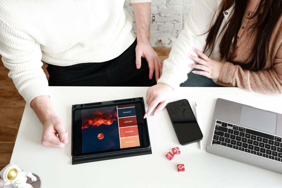 Overhead image of two people at a desk working on their ipad and laptop.