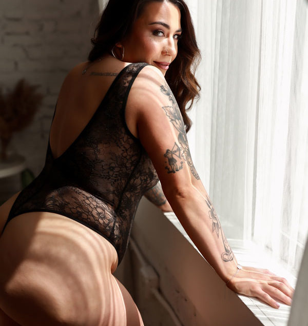 Woman leaning on window looking over shoulder in black lace bodysuit.