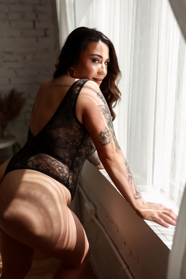 Woman leaning on window looking over shoulder in black lace bodysuit.