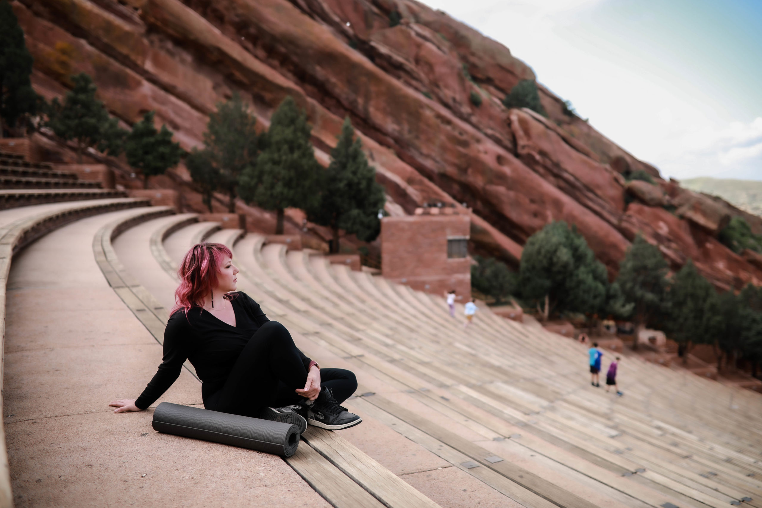 Pilates instructor sitting at Red Rocks Amphitheater with a yoga mat