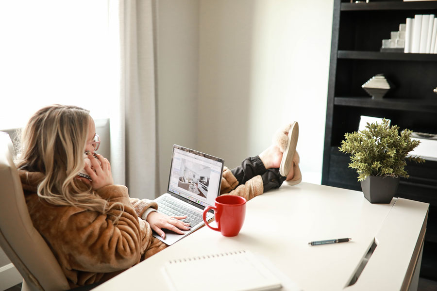 Woman in bathrobe with feet up on desk working on laptop