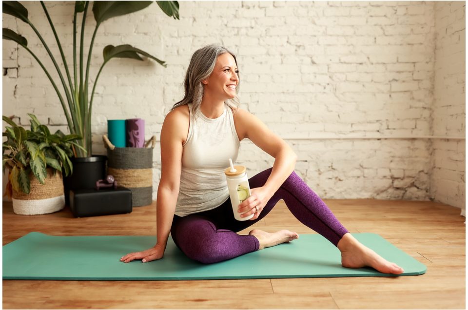 Woman sitting on a yoga mat smiling with a beverage in hand during her branding session.