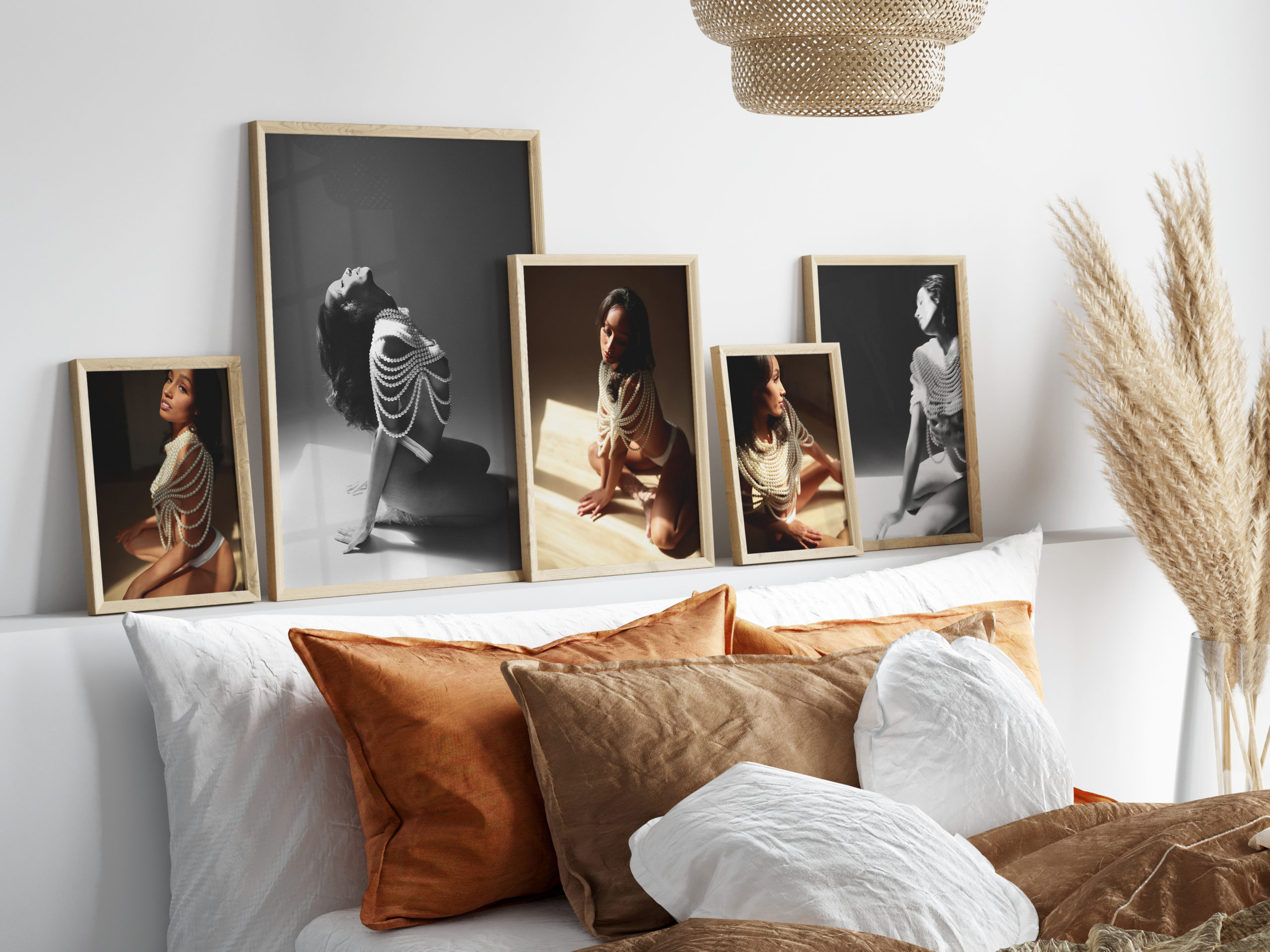 Artistic boudoir photos in monochrome on display above a bed with earth-toned pillows and decor.