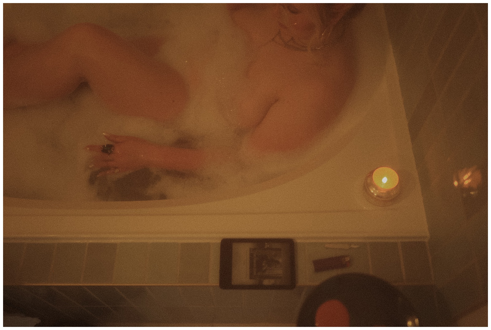 A person relaxing in a reverie in a candlelit bubble bath.