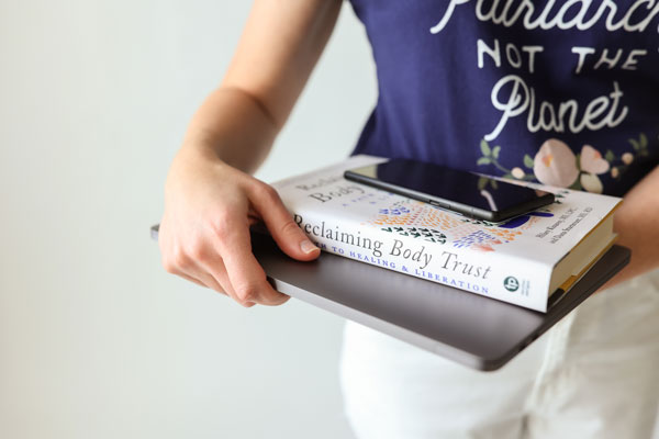 A Denver psychologist holds a book titled "reclaiming body trust" with a smartphone on top of it.