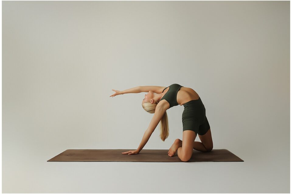 Person in athletic wear performs a yoga pose on a mat, with one arm extended and bent backward.