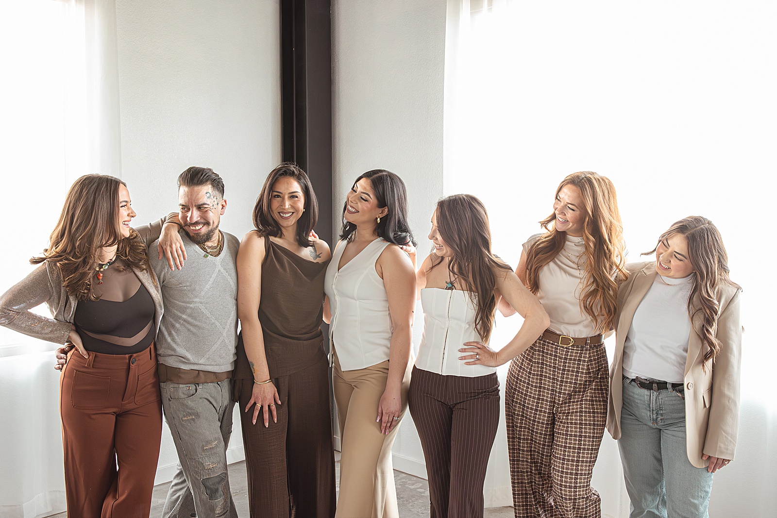 Seven people stand side by side indoors, their body language relaxed and friendly as they smile at each other, all dressed in neutral and earth-toned outfits—perfect for Denver branding photography.