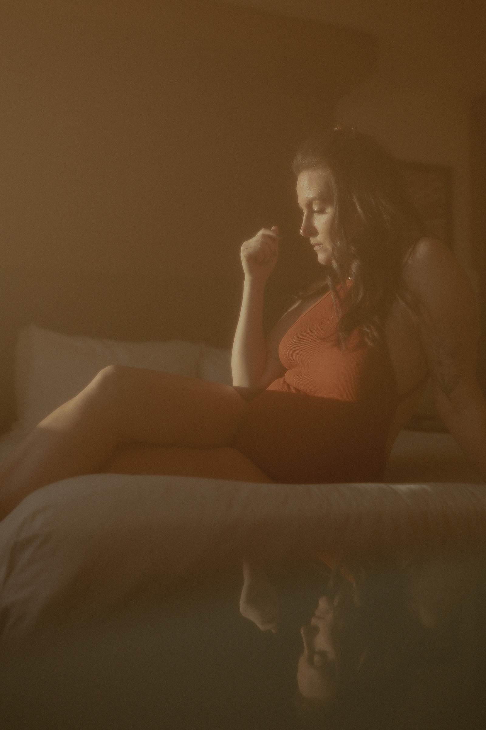 A woman in a rust-colored bodysuit striking a boudoir pose while sitting on a bed.
