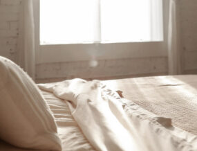 Sunlight filtering through sheer curtains onto an unmade bed.