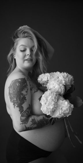 Topless pregnant woman holding flowers with hand in hair.
