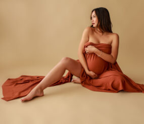 Pregnant woman sitting on floor wrapped in fabric.