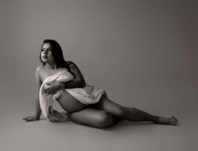 A black and white artistic portrait of a tattooed woman posing with a draped cloth.