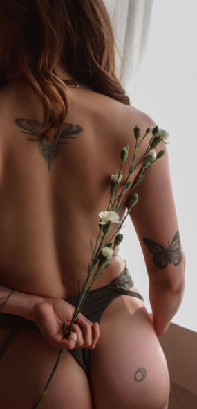 Woman holding flower behind her back with tattoos on her back.