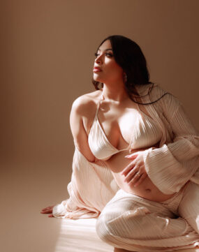Pregnant woman in silk outfit posing on floor.