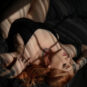 Red haired woman in black bodysuit laying in sun patch in bed.