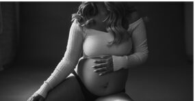 A pregnant woman in a white top posing for a series of serene black and white portraits during her Denver Maternity Session.