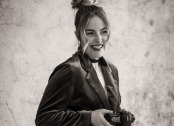 Woman smiling in velvet blazer holding a camera.